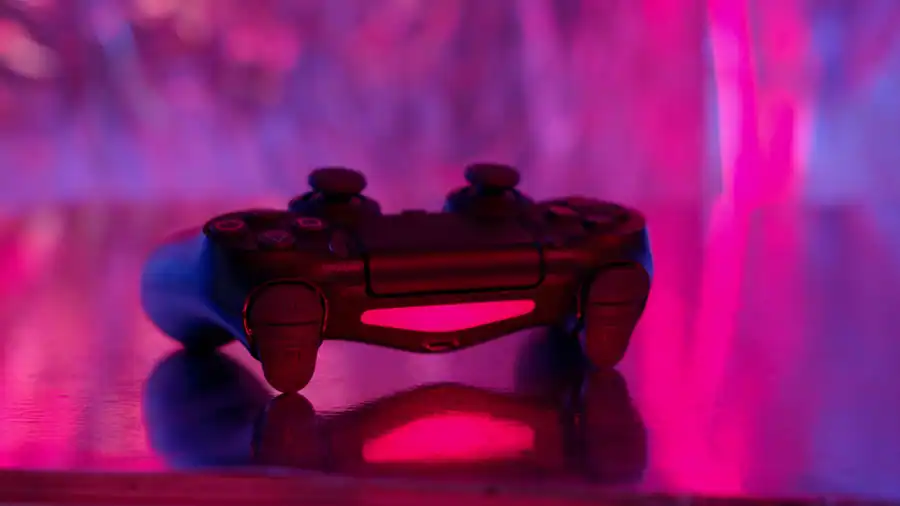 A wireless game controller in focus with a vibrant pink and purple neon background.