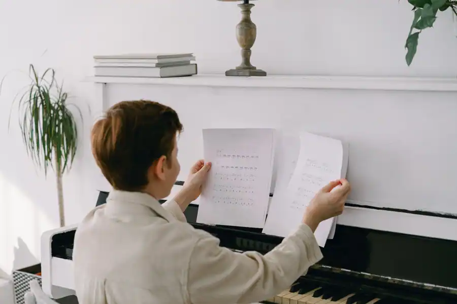 Boy sitting at piano holding music sheets, showcasing learning and skill development indoors.