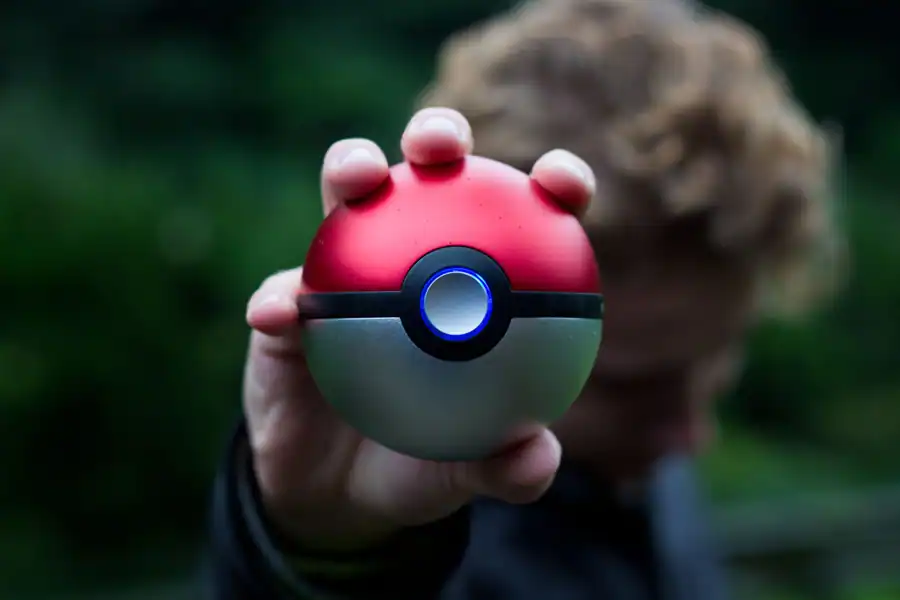 A person holding a Pokeball with a blurred natural background, symbolizing adventure.